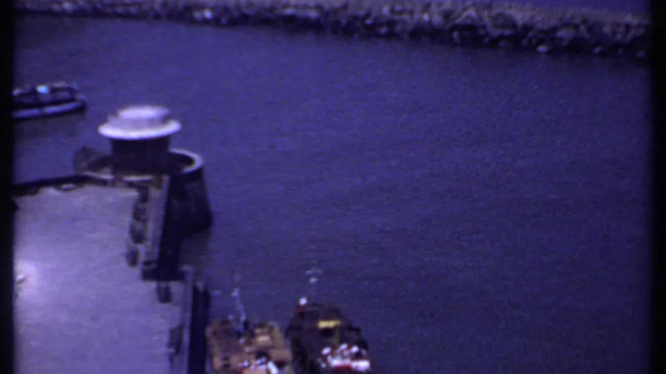 1969 India 8mm harbor view showing blue-toned water, a small boat, dock structure, and stone breakwater.