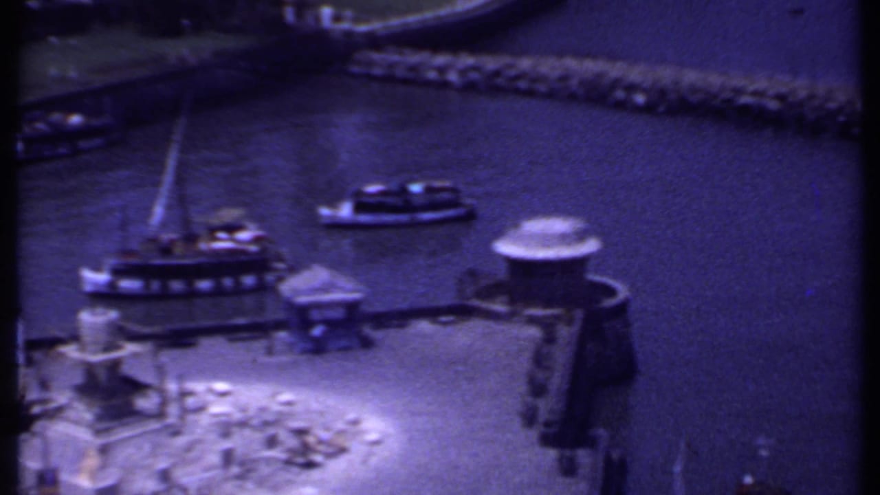 Small boats cluster around a dock with a breakwater across the harbor.