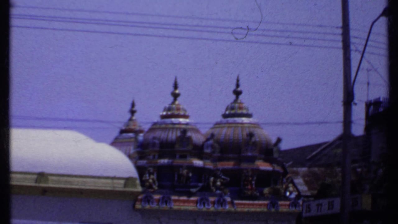 1969 India 8mm frame showing ornate Hindu temple domes and decorative carvings behind a roofline, utility wires, and a street pole.