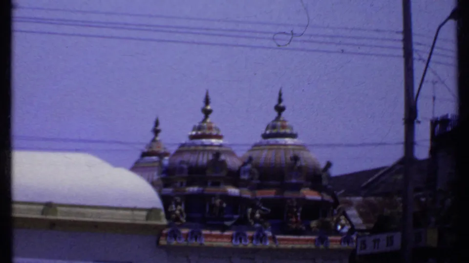1969 India 8mm frame showing ornate Hindu temple domes and decorative carvings behind a roofline, utility wires, and a street pole.
