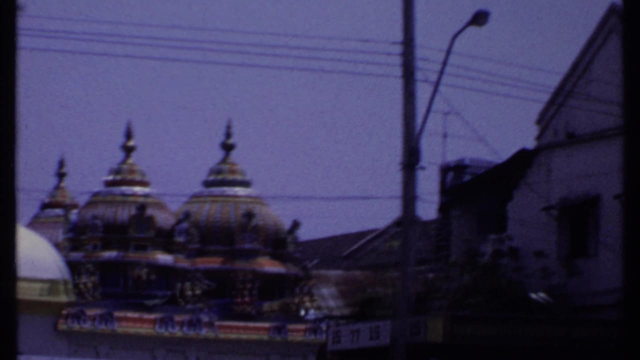 1969 India 8mm frame with ornate temple domes, overhead wires, a street pole, and a dark building edge at the right.