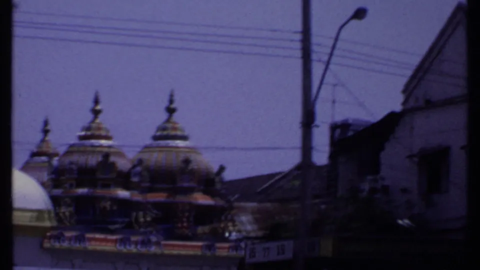 1969 India 8mm frame with ornate temple domes, overhead wires, a street pole, and a dark building edge at the right.