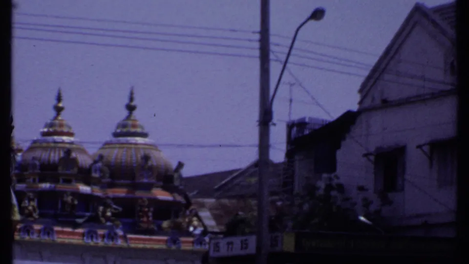 1969 8mm India street view showing colorful temple domes partly obscured by a building, poles, and overhead wires.
