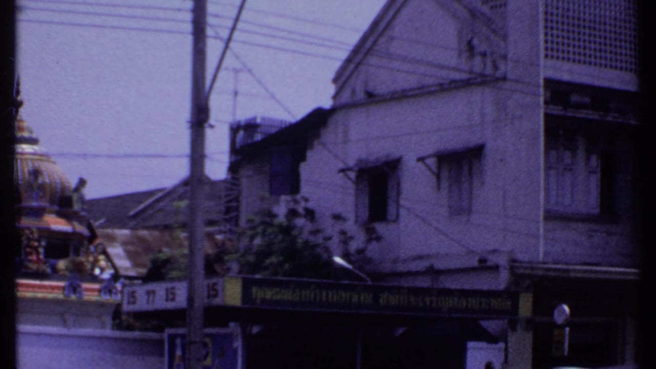 1969 8mm India street view panning past a white building, storefront signage, wires, and the edge of an ornate temple dome.