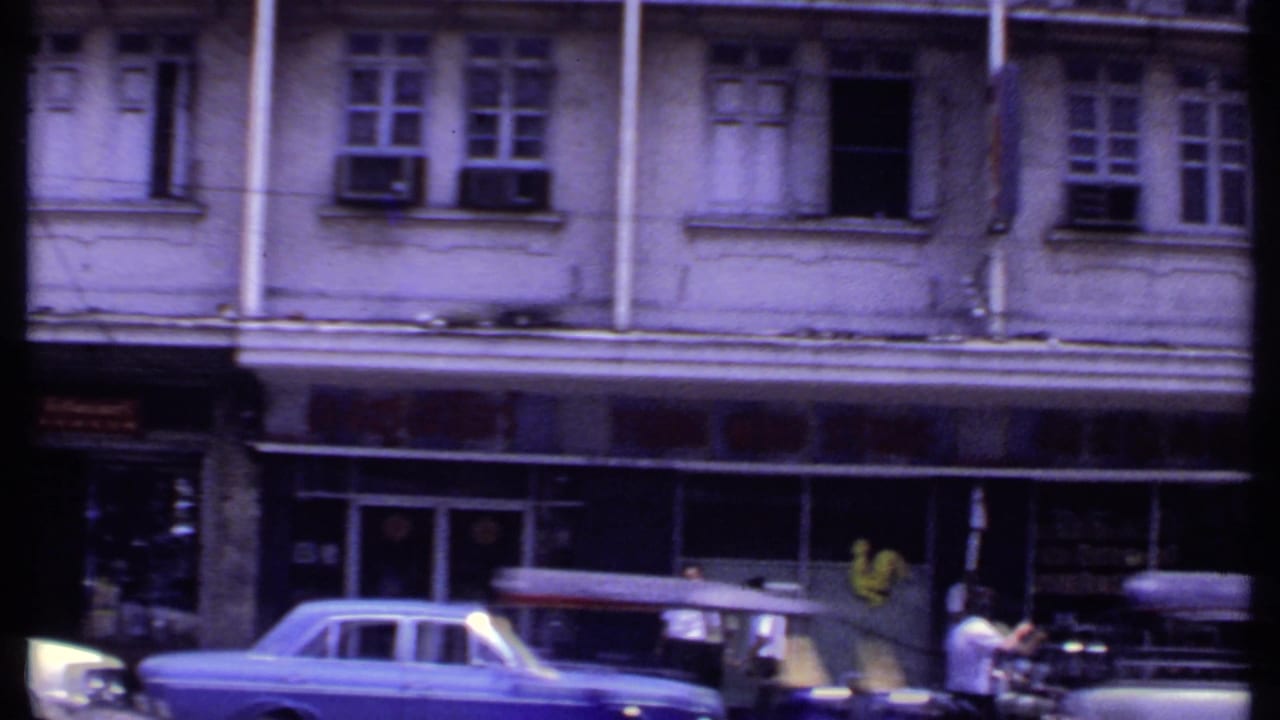 Streetfront with old sedans, pedestrians, awnings, and upper-floor windows.