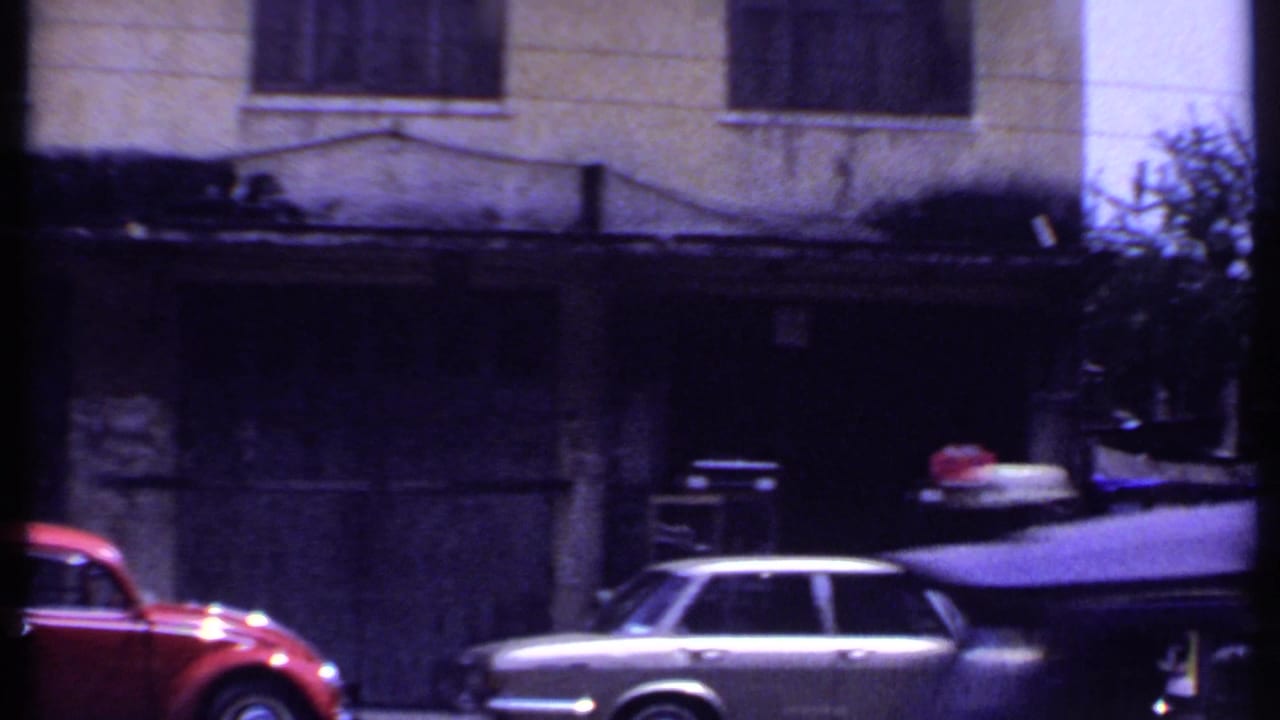 Town street frame from 1969 India showing a red car, a light-colored station wagon, and a darkened building frontage.