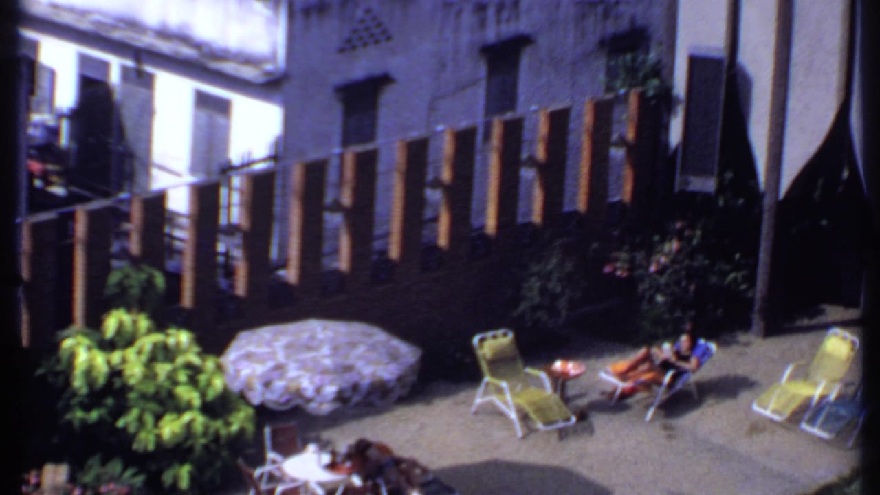 Backyard patio with woman on lounge chair, umbrella, plants, and slat fence.