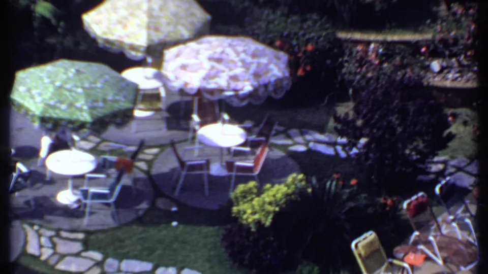 1969 India 8mm frame showing a sunlit patio with green, yellow, and purple umbrellas over tables and chairs.