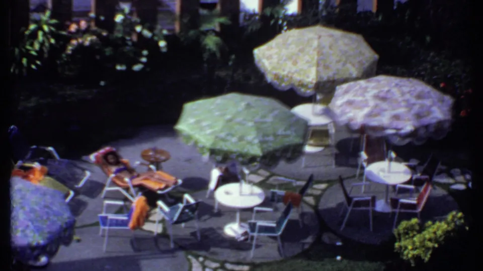 1969 India 8mm view across a shaded patio with floral umbrellas, seating, and a person resting nearby.