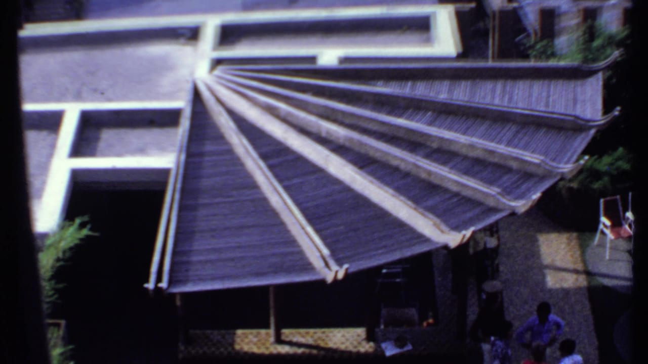 1969 India 8mm frame showing an elevated view of a fan-shaped roof structure with adjoining rooftops and a shaded patio below.
