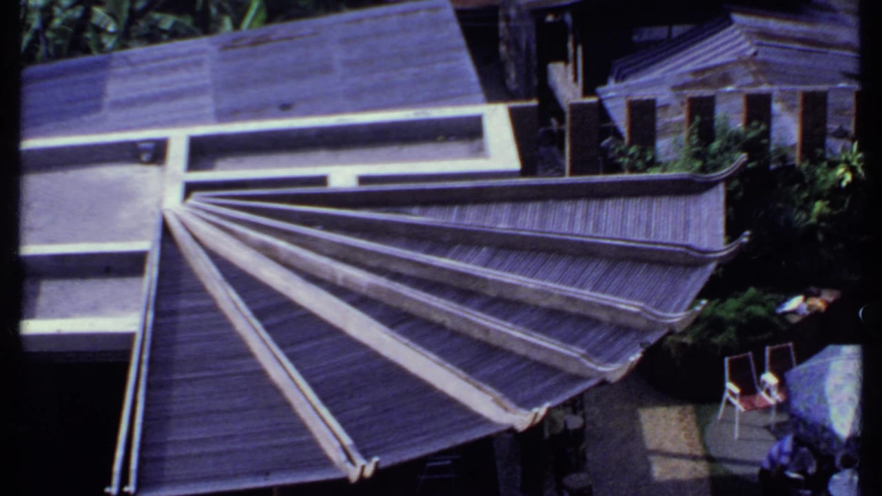 1969 India frame showing the slatted roof from above, with patio chairs, plants, and adjacent residential rooflines in view.