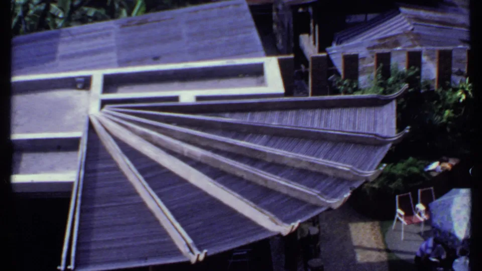 1969 India frame showing the slatted roof from above, with patio chairs, plants, and adjacent residential rooflines in view.