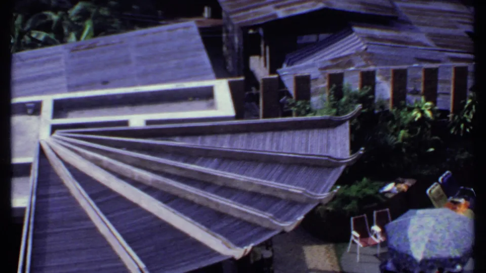 Final 1969 India frame with the fan-shaped roof, adjacent buildings, patio chairs, greenery, and small figures partly visible below.