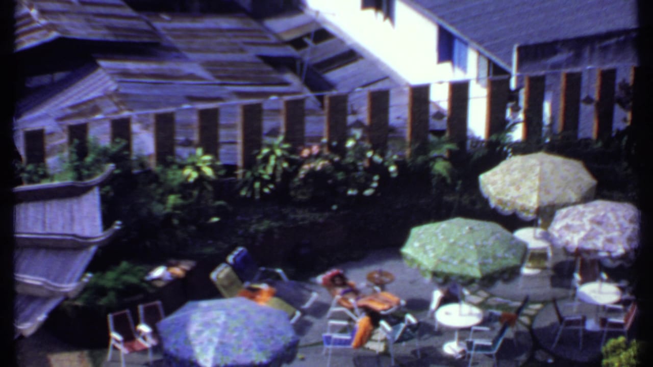 A wider 1969 India terrace view shows several parasols, chairs, small tables, lush plantings, and adults seated in the sun.