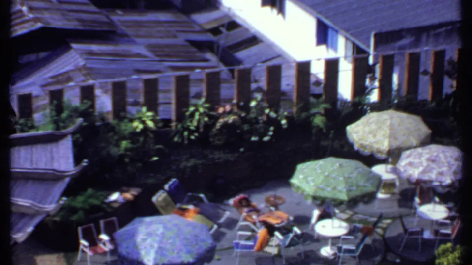 A wider 1969 India terrace view shows several parasols, chairs, small tables, lush plantings, and adults seated in the sun.