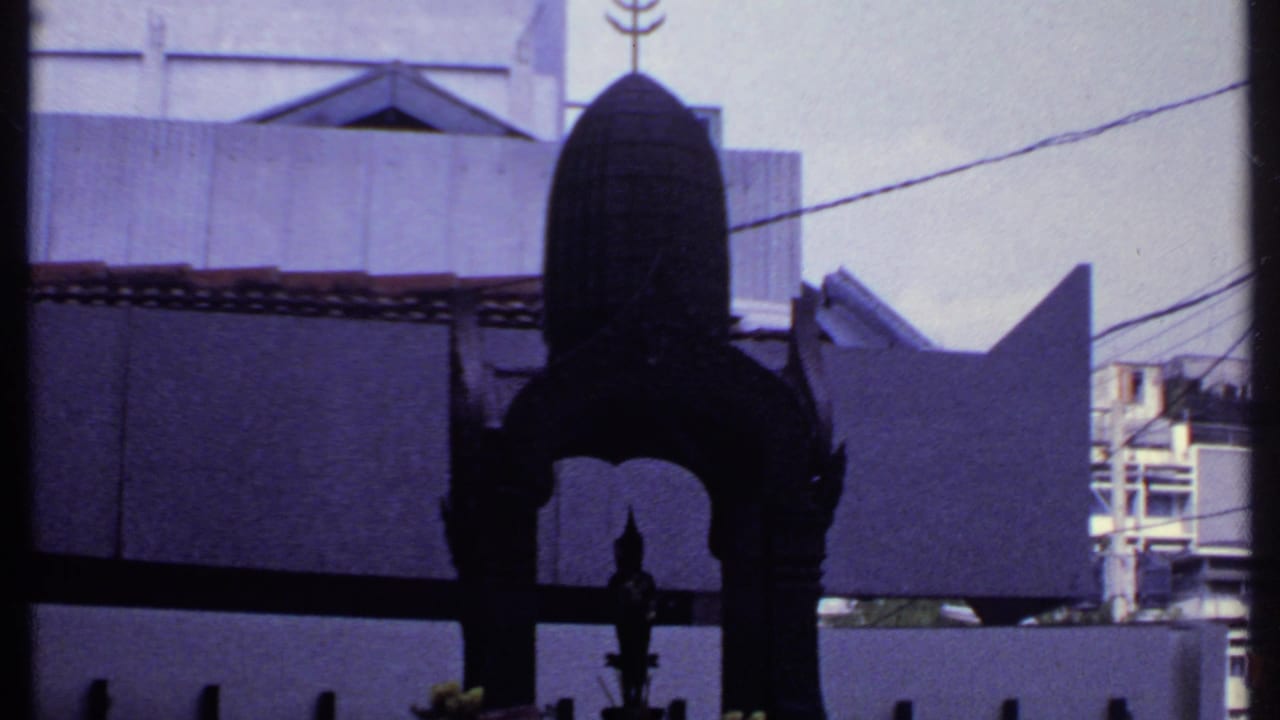 Dark metal shrine centered in front of pale walls, tiled roof edge, and utility wires.