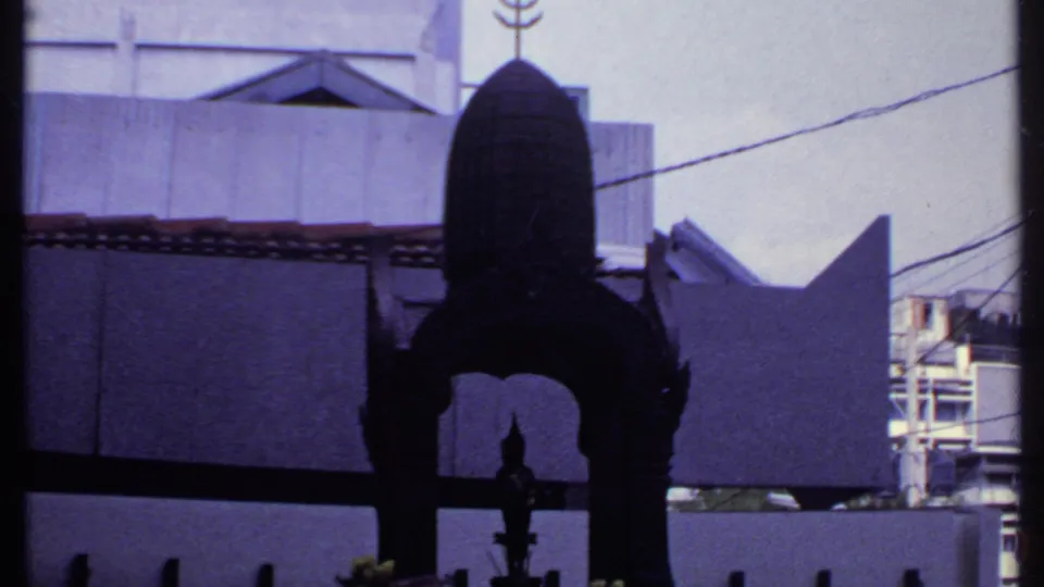 The 1969 India frame centers the arched metal shrine, with a pale concrete wall, roof tiles, wires, and a neighboring structure visible behind.