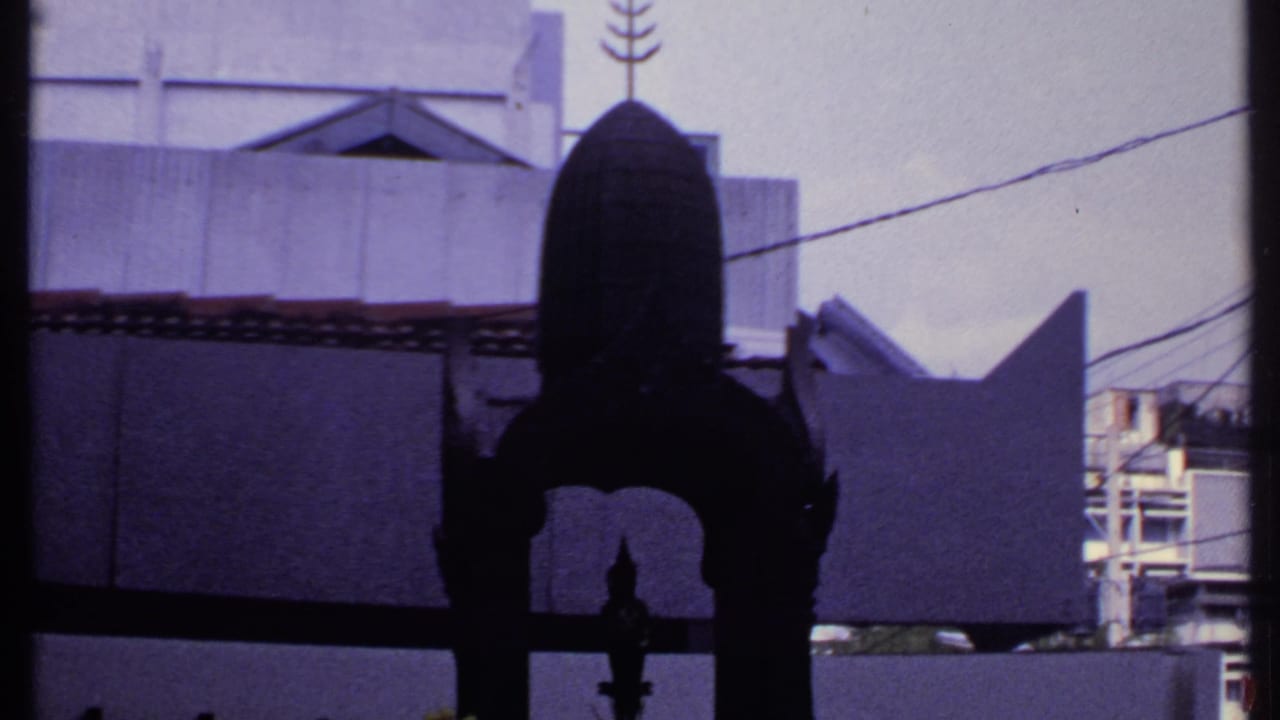 A close 1969 India home-movie view shows the dark arched shrine partially silhouetted before pale walls, roof tiles, wires, and fence points.