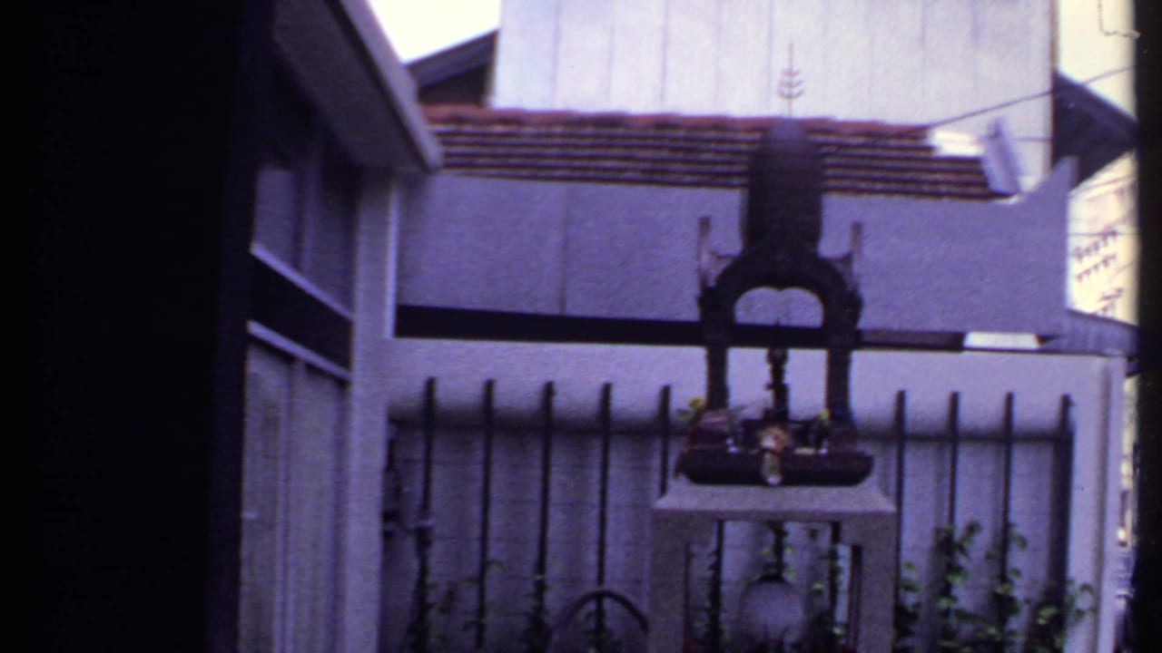 Ornate dark shrine-like object on a pedestal behind a metal fence outside a house.