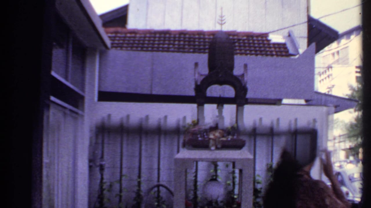 A woman enters the right edge of this 1969 India frame near a fenced shrine-like object in front of a residence.