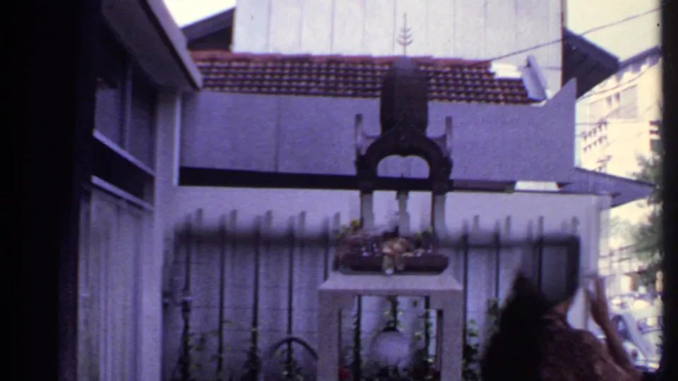 A woman enters the right edge of this 1969 India frame near a fenced shrine-like object in front of a residence.