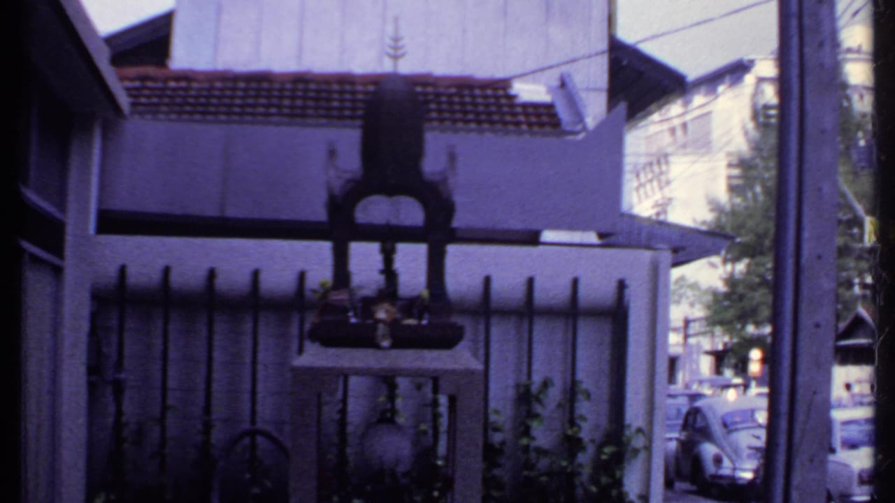 Final 1969 India frame showing the shrine-like object, house exterior, fence bars, plants, and parked cars beyond the street.
