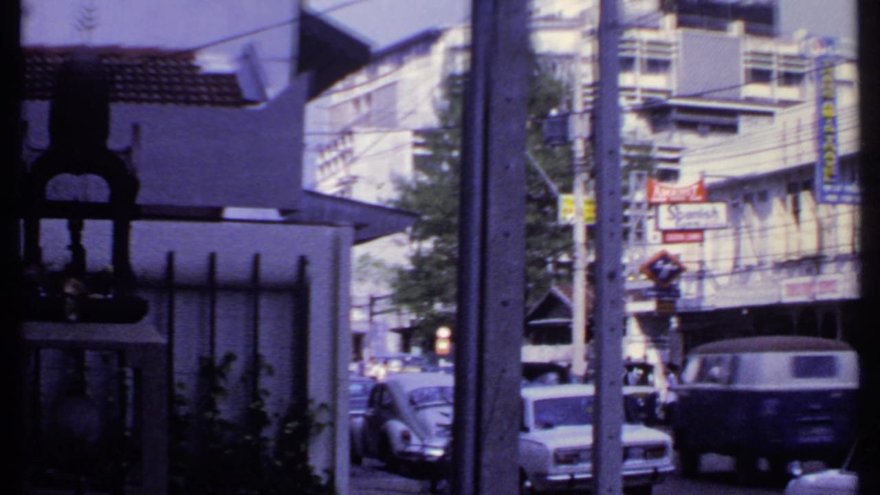 1969 India urban street scene with a Volkswagen Beetle, storefront signage, utility wires, and a foreground post.
