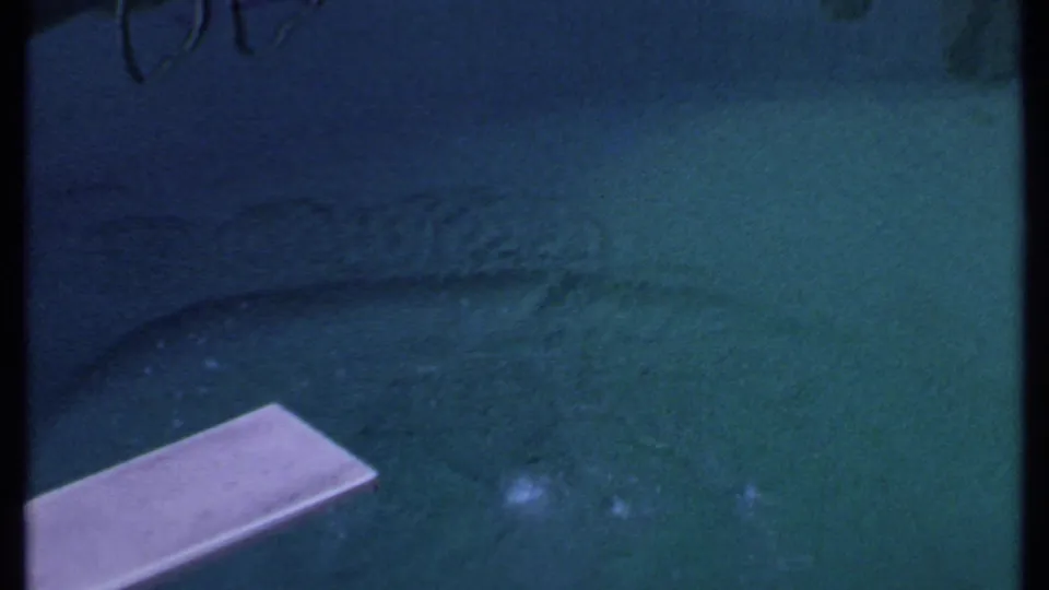 A brief 8mm view shows a green-blue water surface with a pale rectangular ledge or board entering from the lower left.
