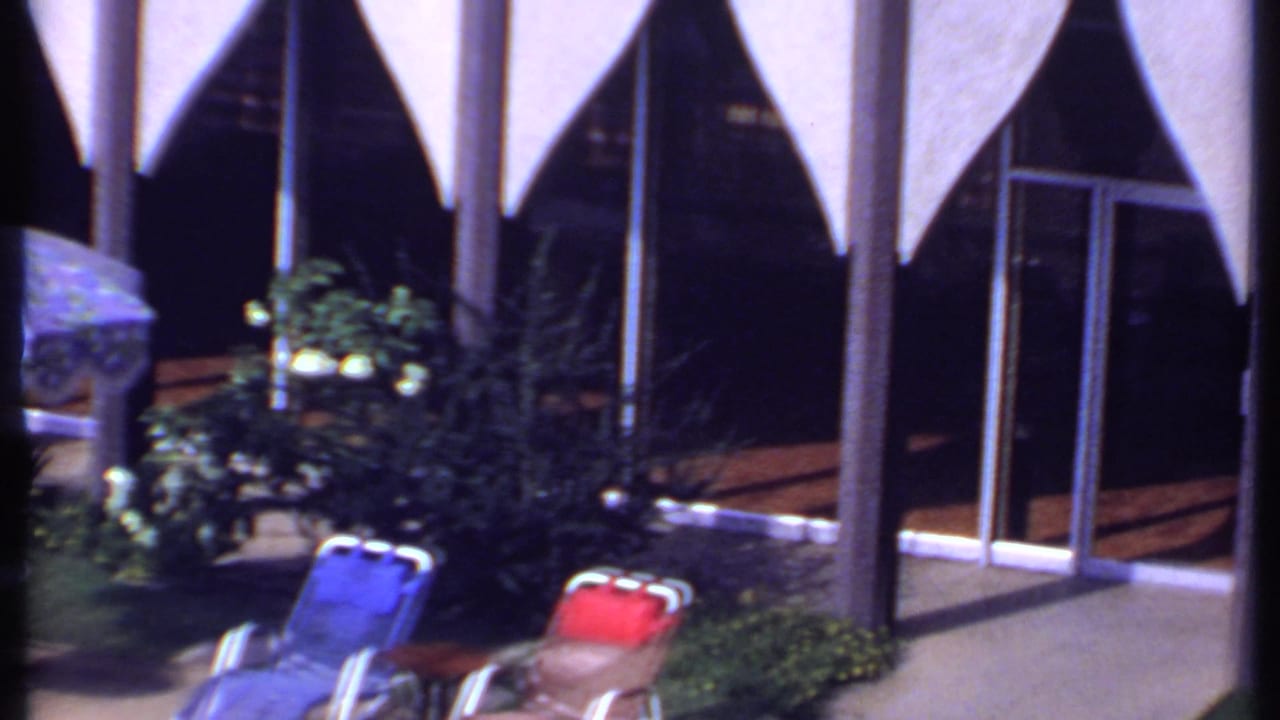The final frame repeats the sunlit building facade with triangular awnings, glass doors, greenery, and red and blue outdoor chairs.