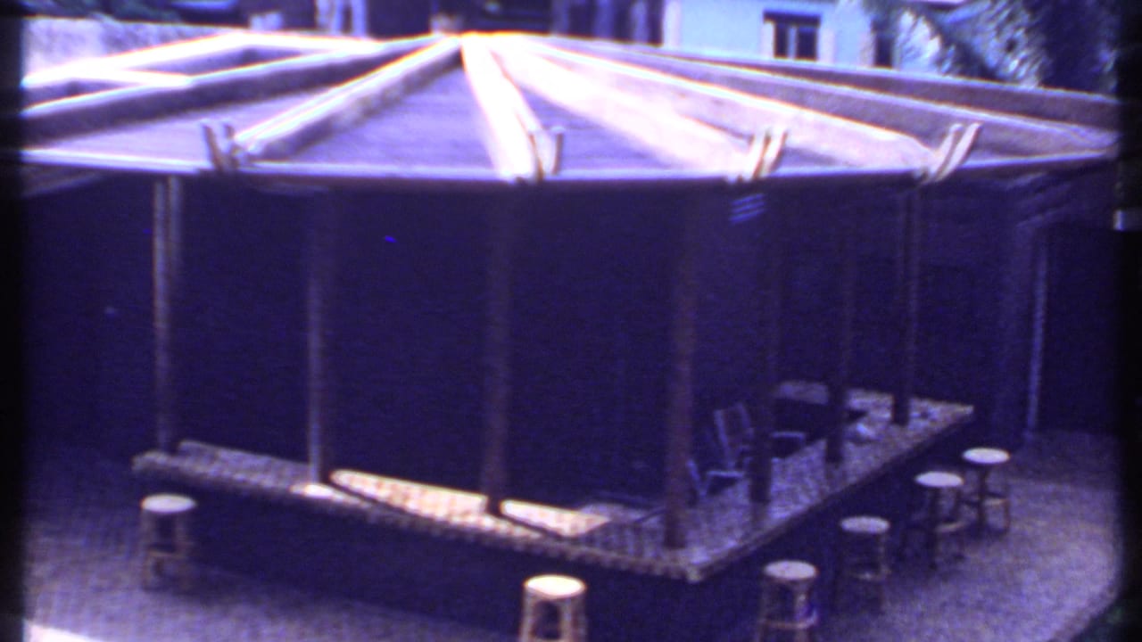 1969 India 8mm view of the outdoor bar from above, with stools, chairs, a raised platform, and surrounding garden paving.