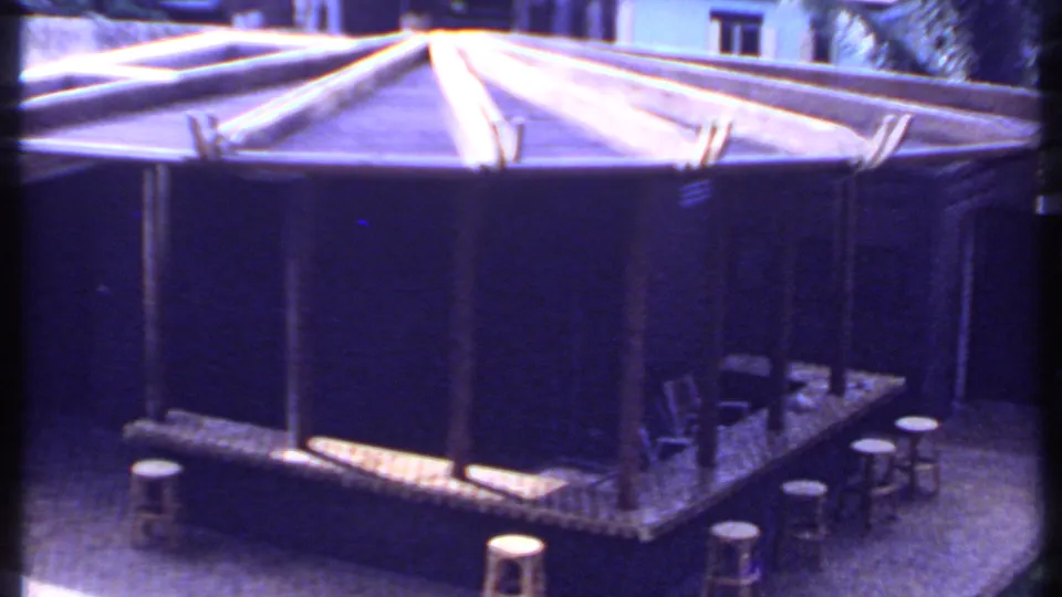 1969 India 8mm view of the outdoor bar from above, with stools, chairs, a raised platform, and surrounding garden paving.