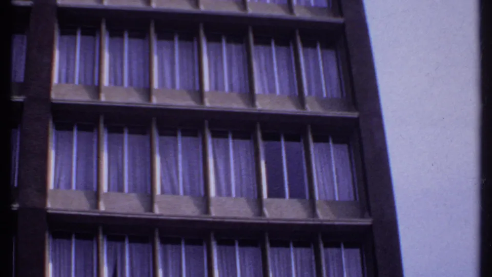 Tilted 1969 India home-movie view of a modern building exterior with stacked rows of curtained windows.