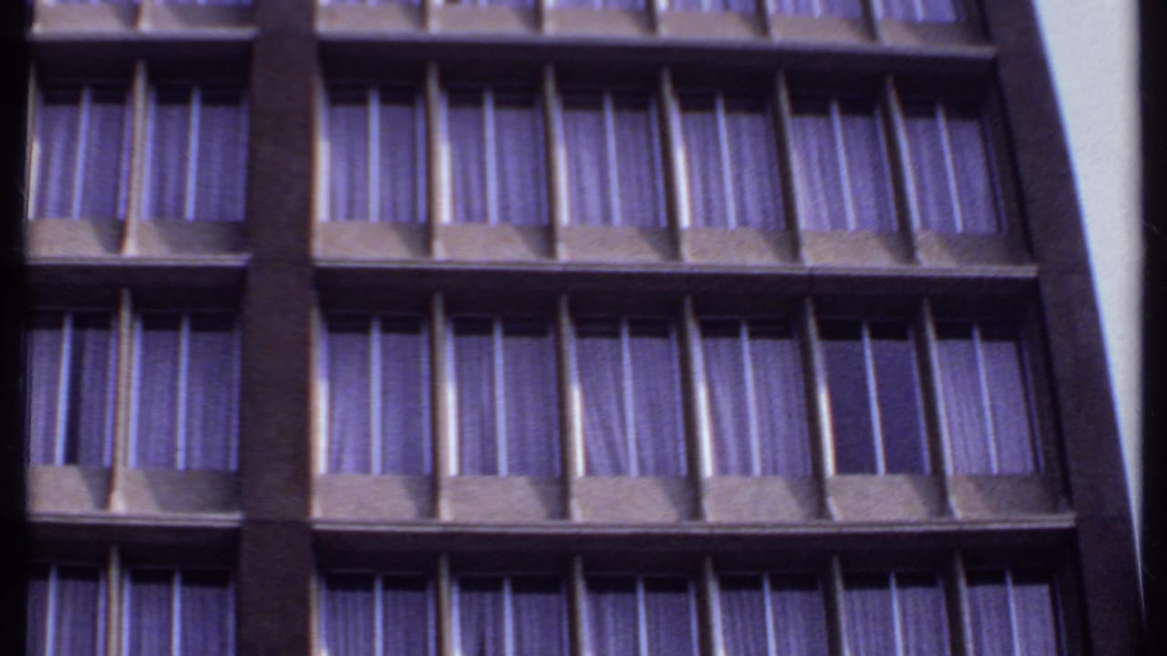 1969 India 8mm frame showing a low-angle section of a high-rise facade with repeated windows, dark supports, and purple drapes.