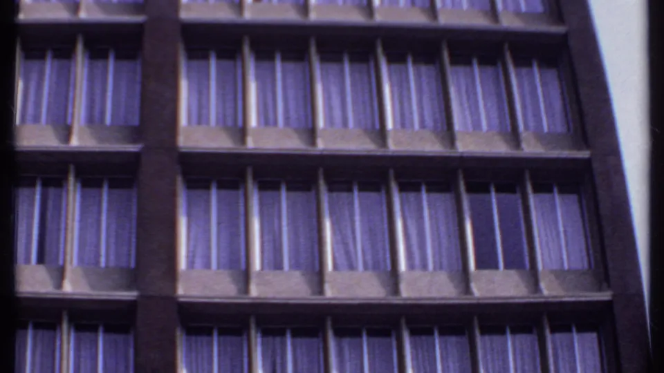 1969 India 8mm frame showing a low-angle section of a high-rise facade with repeated windows, dark supports, and purple drapes.