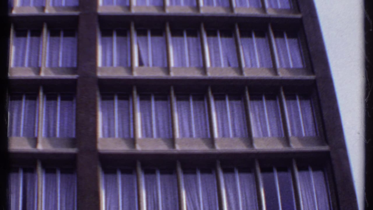 1969 India 8mm frame looking upward at repeated window bays, dark framing, and purple-tinted drapes on a high-rise facade.