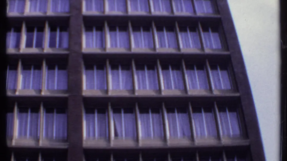 1969 India 8mm frame of a high-rise exterior with dense rows of windows, purple drapes, and dark structural bands.