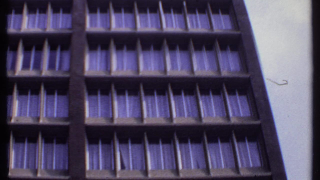 1969 India 8mm frame showing an upward-angled view of a concrete motel facade with repeated window bays and purple-tinted curtains.