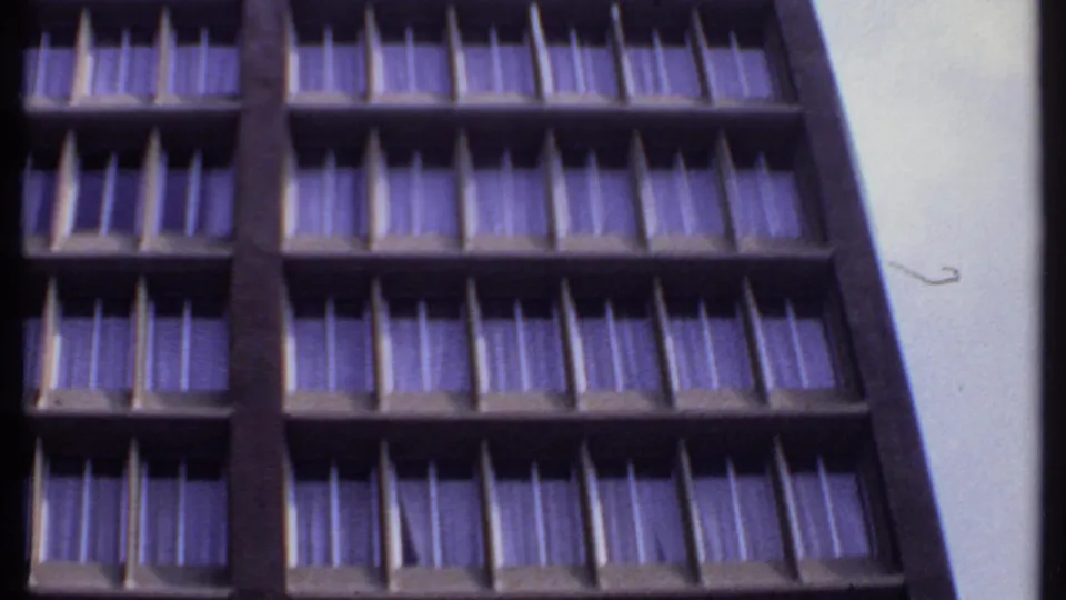 1969 India 8mm frame showing an upward-angled view of a concrete motel facade with repeated window bays and purple-tinted curtains.
