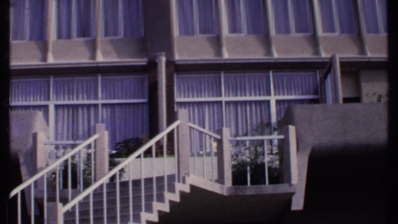 White staircase and balcony railings in front of large curtained windows.