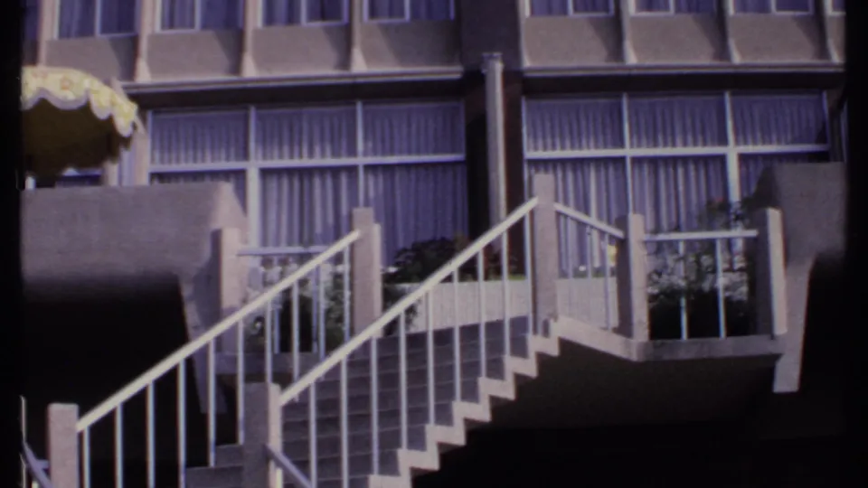 1969 India 8mm frame showing concrete balconies, white stair railings, curtained windows and a yellow umbrella or awning at the edge.