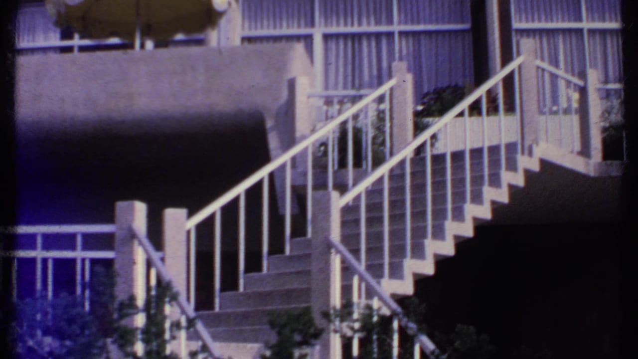 Exterior stairway with concrete railings, balcony windows, and shrubs.