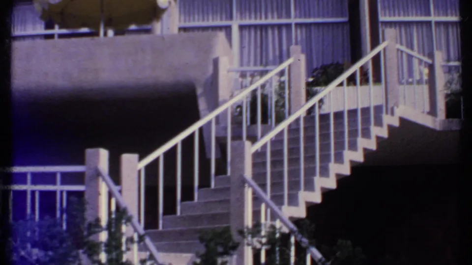 1969 India 8mm frame showing an exterior stairway, concrete railings, balcony glazing, and greenery near a building facade.
