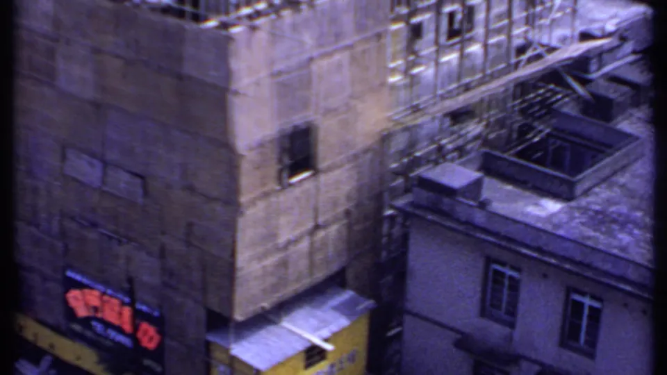 1969 India 8mm frame showing neighboring buildings, rooftop features, scaffolding along a concrete wall, and a yellow structure below.