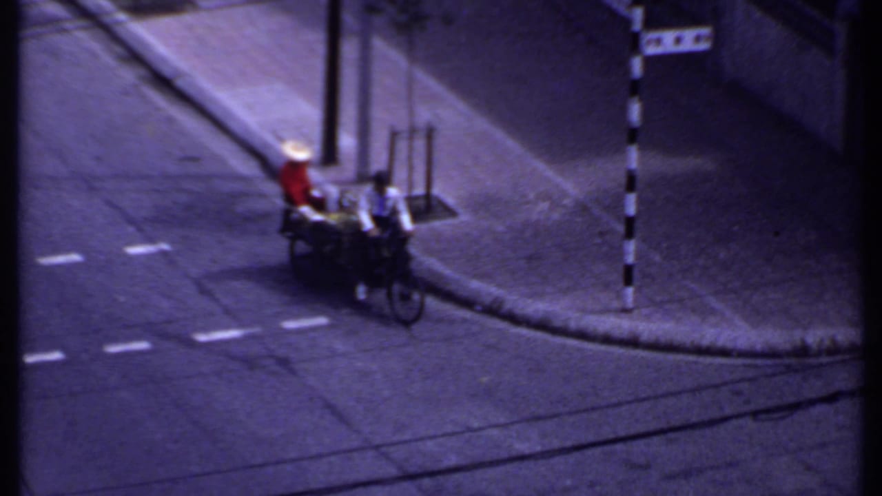 Rickshaw or vendor cart moves along a paved street near a striped pole.