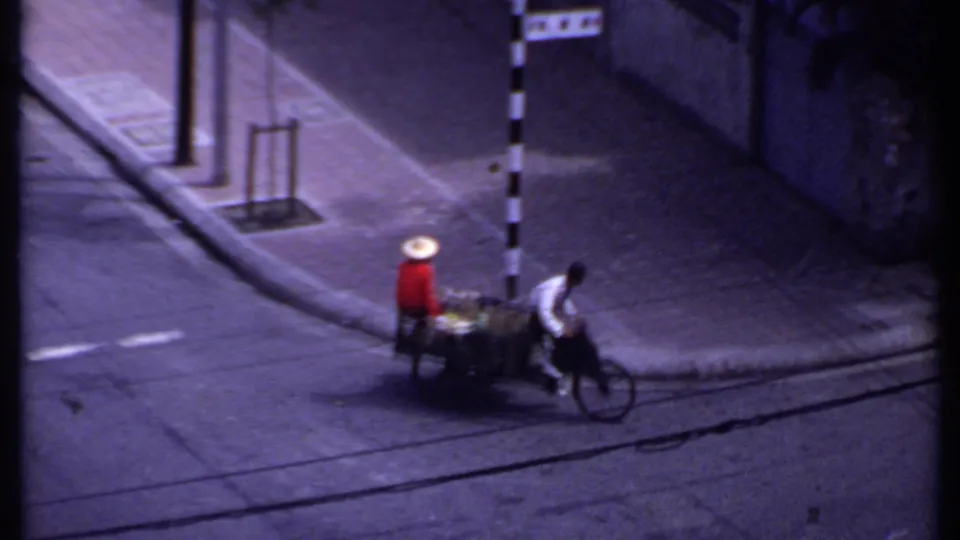 1969 India street frame with a cart passenger or vendor in red and a man cycling past a black-and-white striped pole.