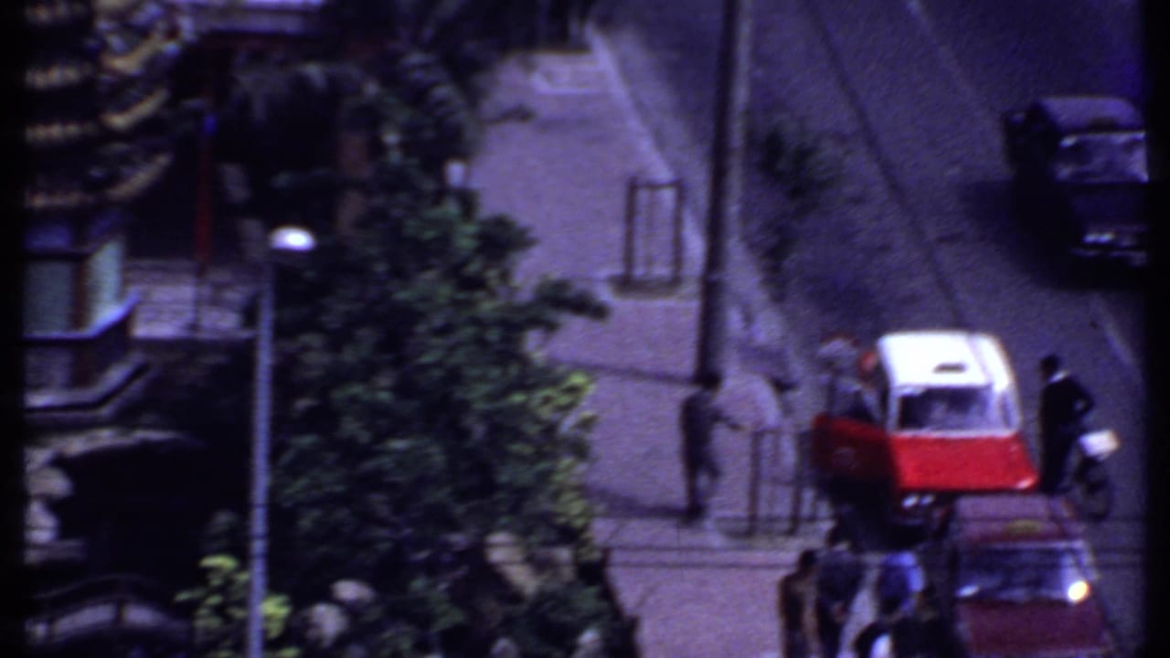 Elevated street view with a red-and-white car, pedestrians, trees, and part of a tiered roof structure.