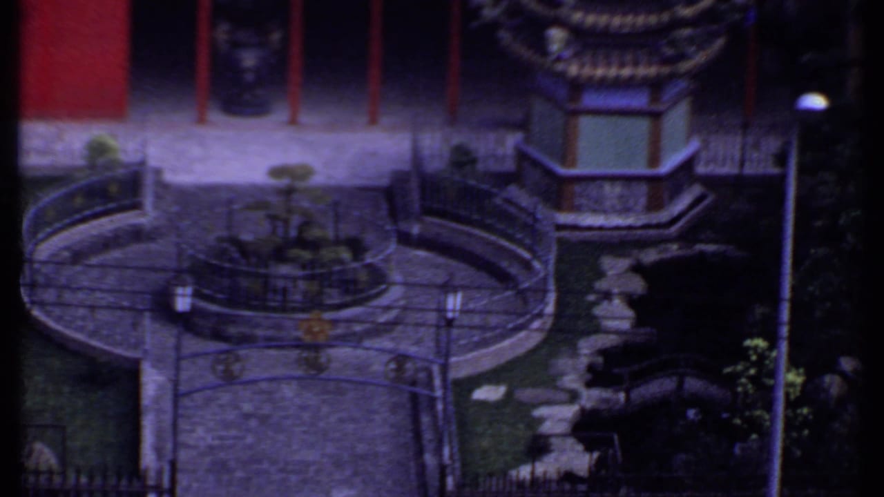 Elevated view of a garden courtyard with red walls, curved railings, stone paving, and a small ornament.