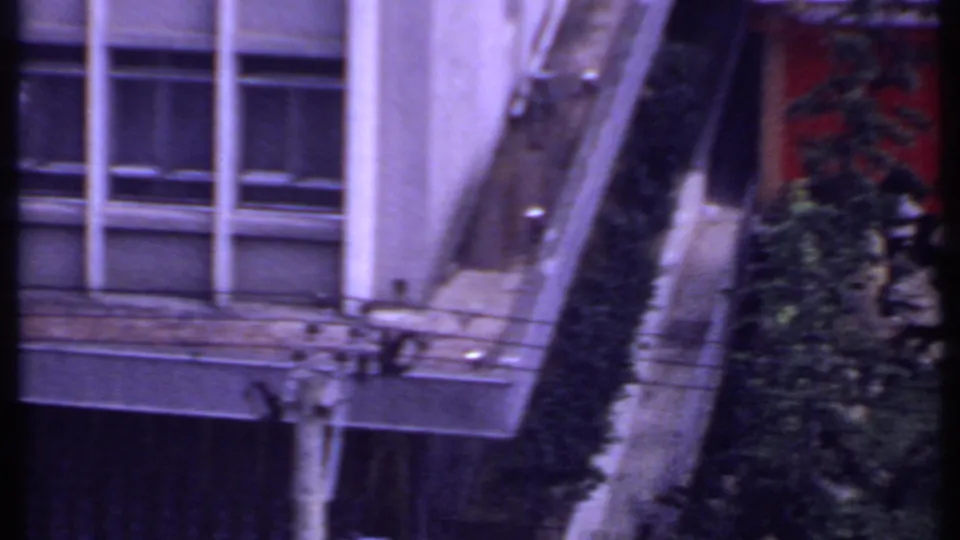 1969 India 8mm frame showing a building facade, windows, sloped roof edge, hedge, and nearby garden plantings.