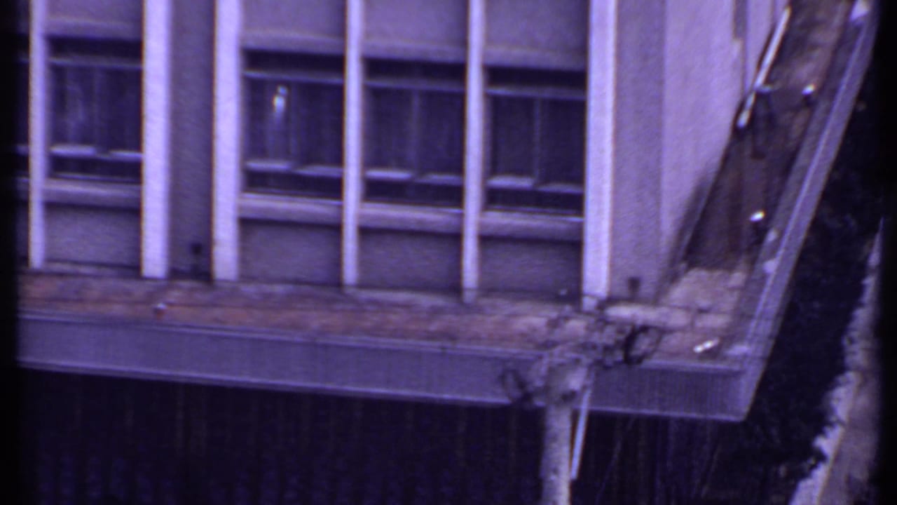 1969 India 8mm frame showing part of a modern office facade with windows, white columns, balcony edge, and dark wall panels.