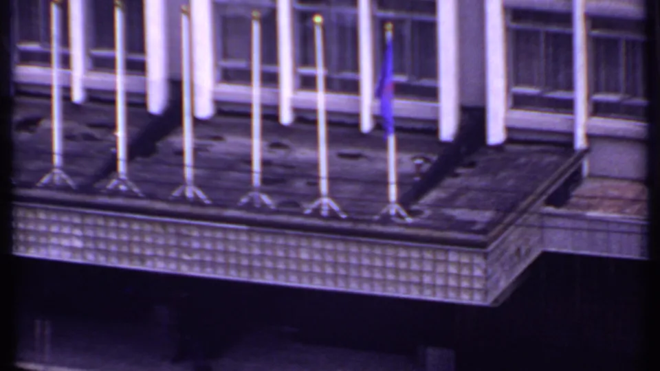 1969 India 8mm frame showing a building rooftop lined with flagpoles, including a blue flag, above large window bays.